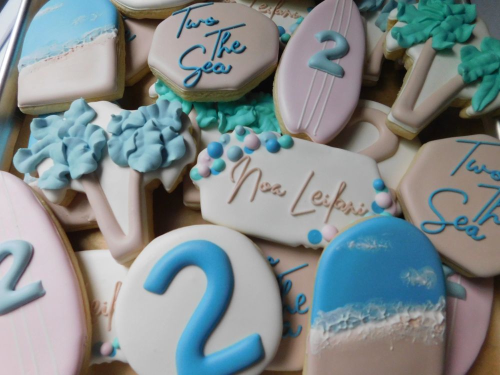 Beach birthday cookies with surfboards, palms, and sandy shore icing