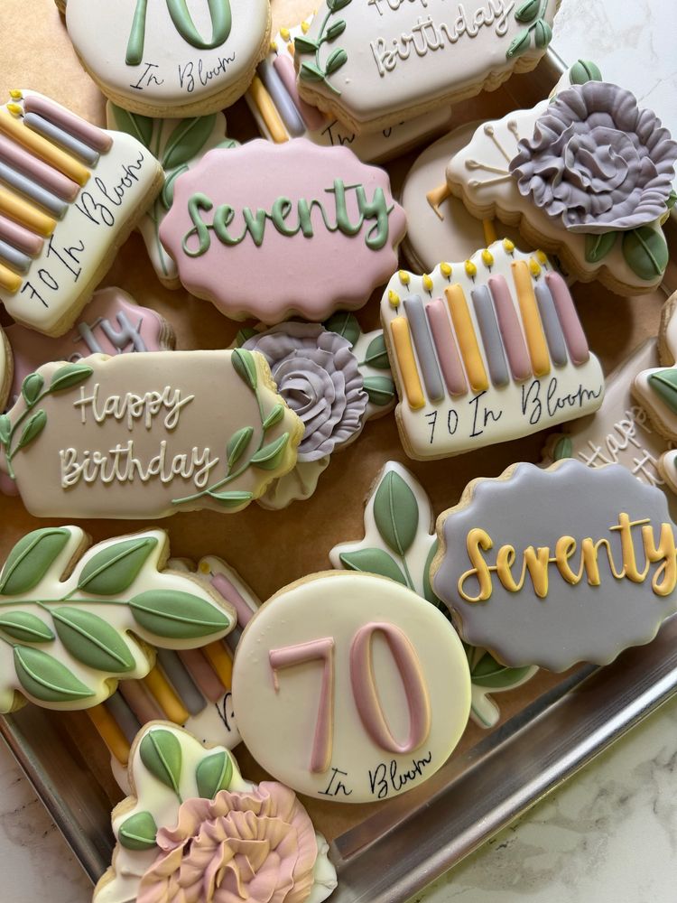 Soft pastel seventieth-birthday cookies with candles, roses, and leafy plaques