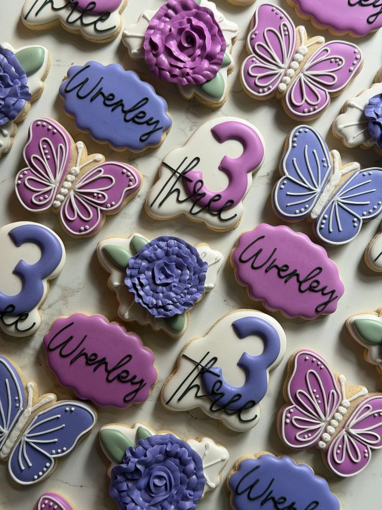 Purple and periwinkle butterfly, rose, and number-three sugar cookies arranged on marble