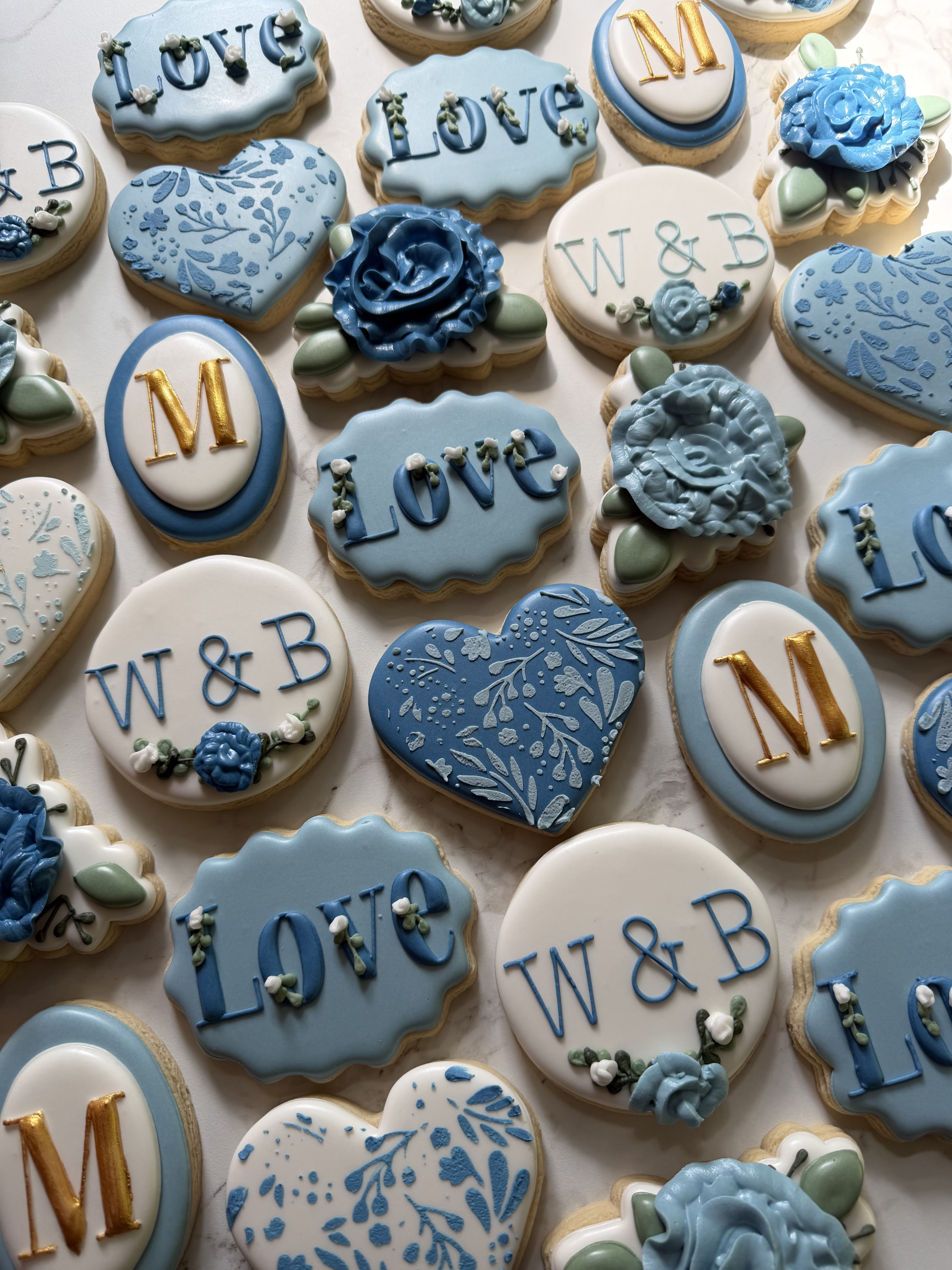Dusty blue wedding cookies lettered Love and W and B, with gold monograms and sugar roses