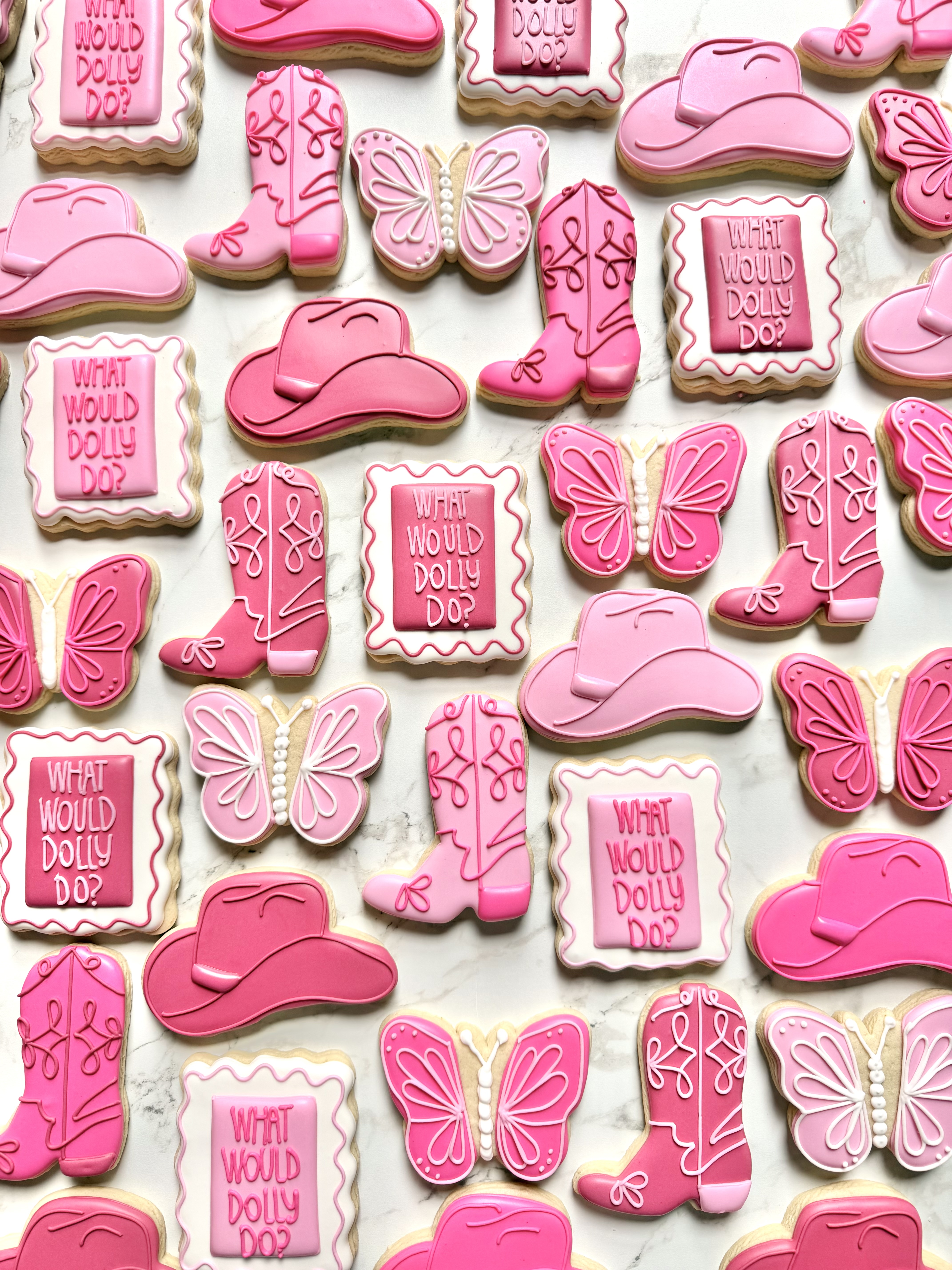 Pink cowboy cookies with boots, hats, butterflies, and What Would Dolly Do plaques